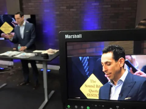 A studio field monitor shows Jess Todtfeld presenting, while he stands at a table on the set behind it