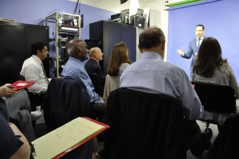 Jess teaching at a blue studio backdrop while participants with notebooks watch