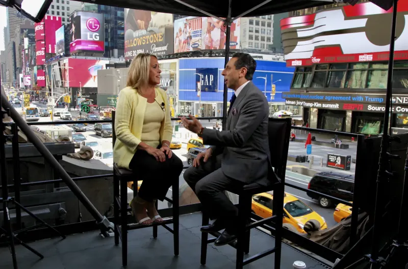 Jess Todtfeld interviewing a client on a Times Square set, taxis and billboards below
